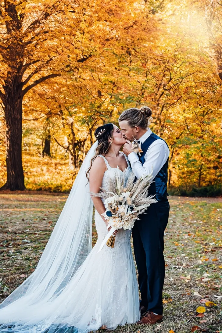 bride and groom kissing in front of beautiful fall foliage
